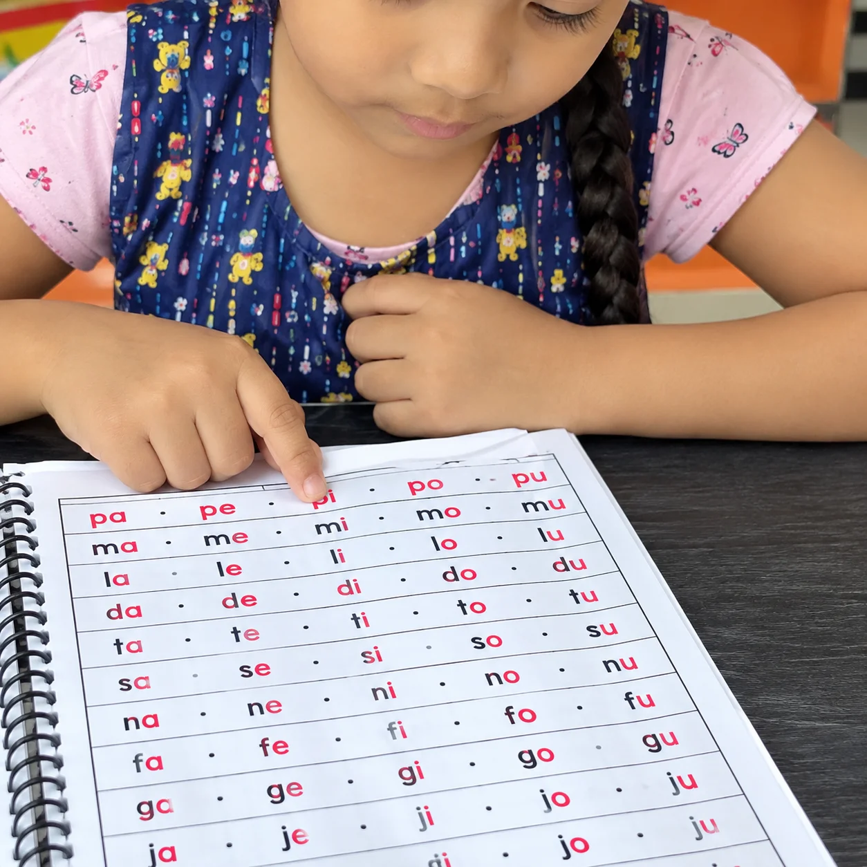 Niña repasando listas de sílabas con el dedo en una ficha del kit