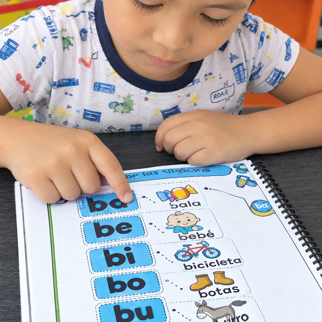 Niño señalando las sílabas ba, be, bi, bo, bu en el cuaderno del kit